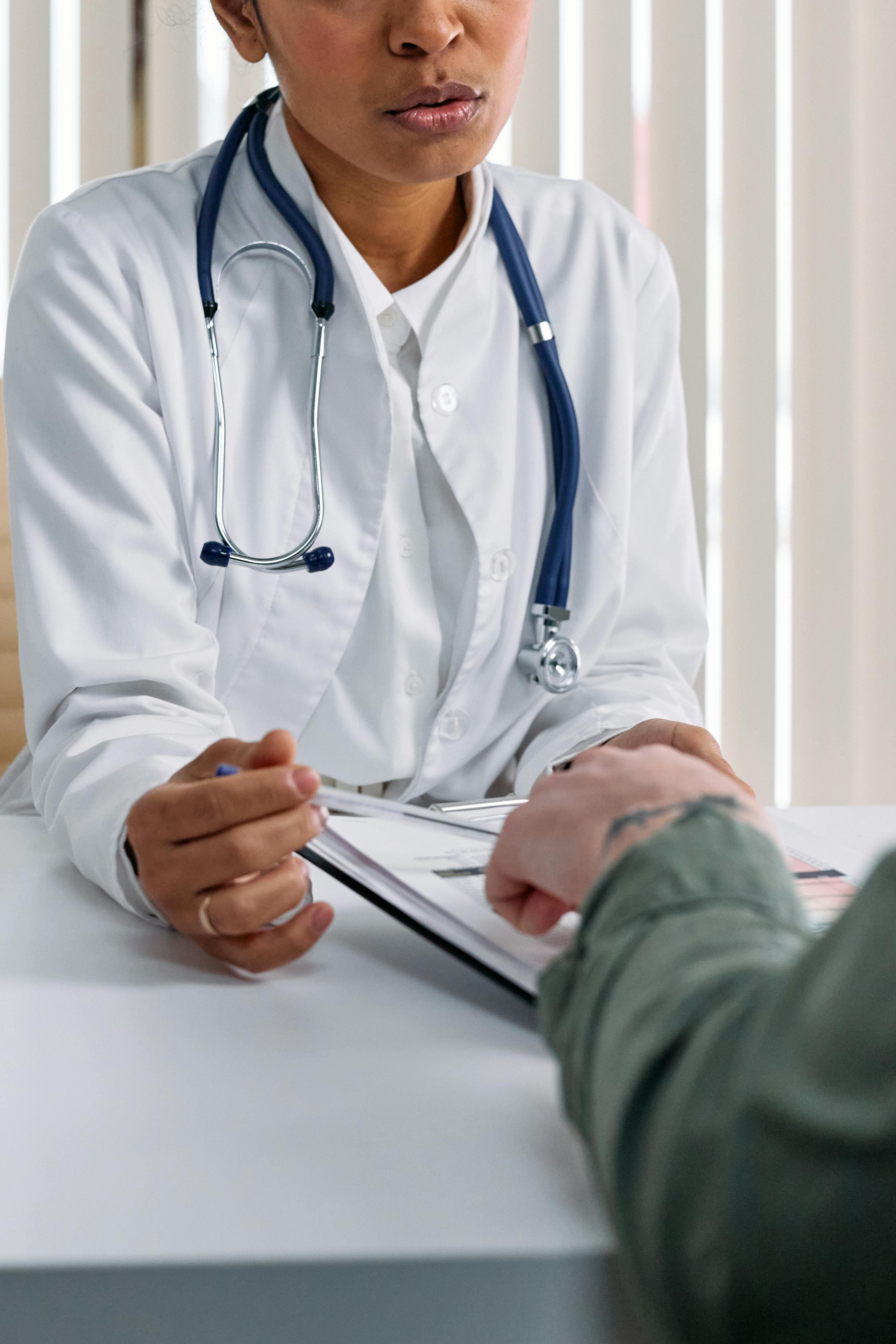 Médica em jaleco revisando documentos com paciente à mesa — consulta — MDT Saúde Ocupacional